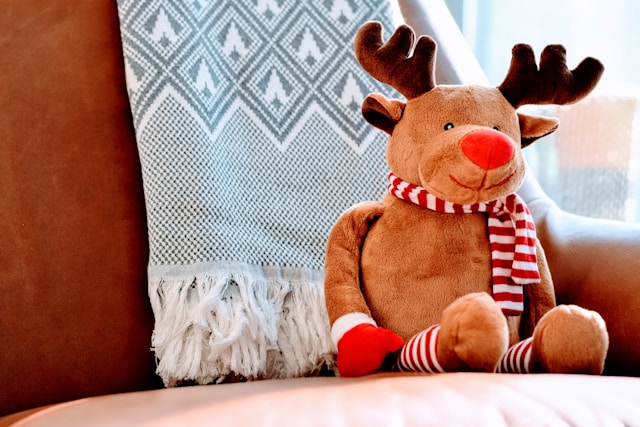 fluffy brown reindeer toy with scarf on it. it sits on a quilted bed